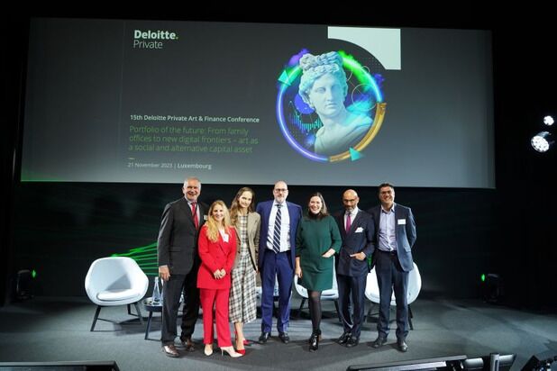 A group of seven people stands on a stage at the 15th Deloitte Private Art & Finance Conference in Luxembourg. Behind them is a large screen displaying conference details, including the date, November 21, 2023. The stage is set with chairs and illuminated with green lighting.